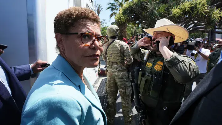 L.A. Mayor Karen Bass stands in front of a U.S. Border Patrol federal agent at MacArthur Park on Monday in Los Angeles. (Image Credit: Damian Dovarganes/AP)