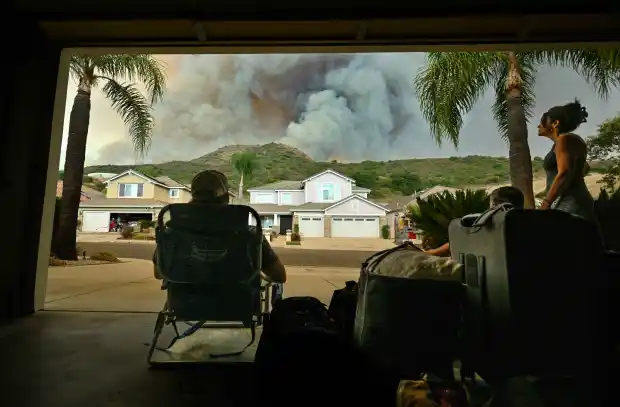 Jake Spillane, left, his father, Jim Spillane, center, and mother, Lori Spillane, sit in their garage with suitcases, ready to evacuate, as they watch smoke from the Airport Fire rise behind Meander Lane in Trabuco Canyon, CA, on Monday, Sept. 9, 2024. (Photo by Jeff Gritchen, Orange County Register/SCNG)