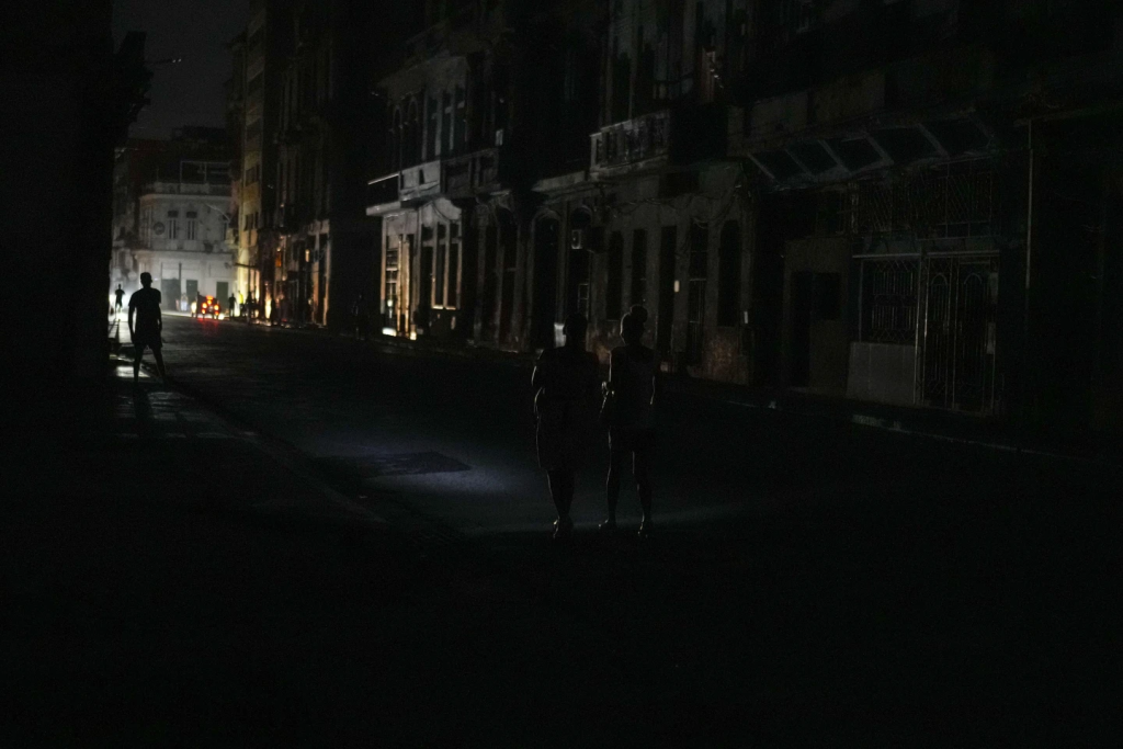 Cuba Power Crisis: Blackouts Continue to Plague the Island 3 Residents walk along a street during a massive Cuba power outage in Havana, Cuba, Friday, Oct. 18, 2024. (Image Source: Ramon Espinosa/AP)