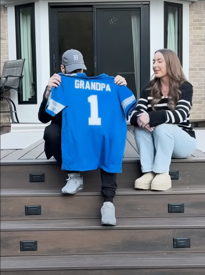 In the emotional music video for "Temporary," Eminem includes a touching scene where Hailie surprises her father with a blue jersey that reads “#1 Grandpa” alongside a sonogram of her unborn child. (Image Source: YouTube @eminem)