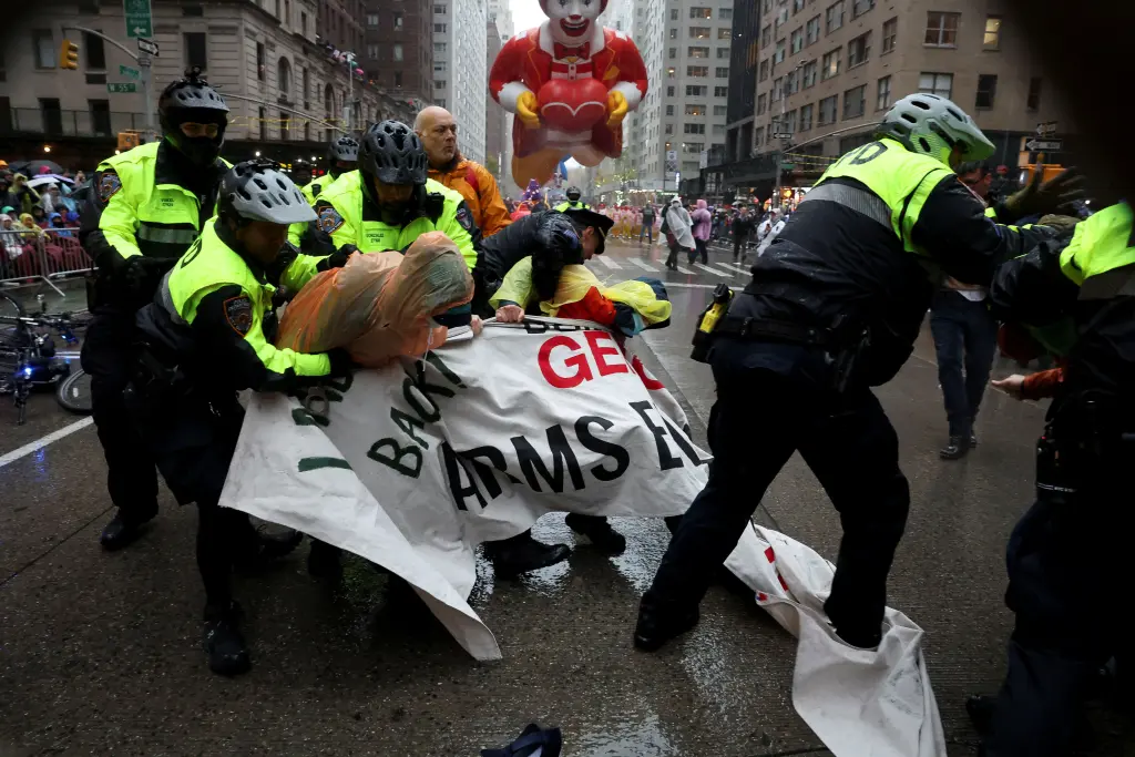 Thanksgiving parade protesters being pulled away and flipped over onto their stomachs to be handcuffed while others willingly stood up and walked with police away from the parade. (Image Credit: REUTERS)