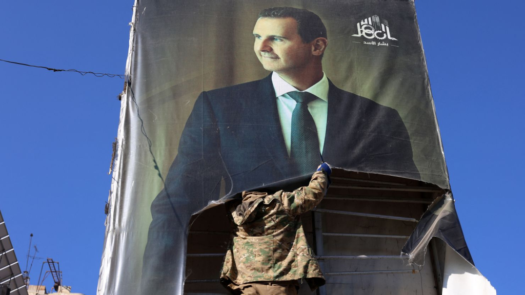 Rebel fighters tears down a portrait of Syria's President Bashar al-Assad on November 30, 2024. (Image Credit: Mohammed Al-Rifai/AFP/Getty Images)