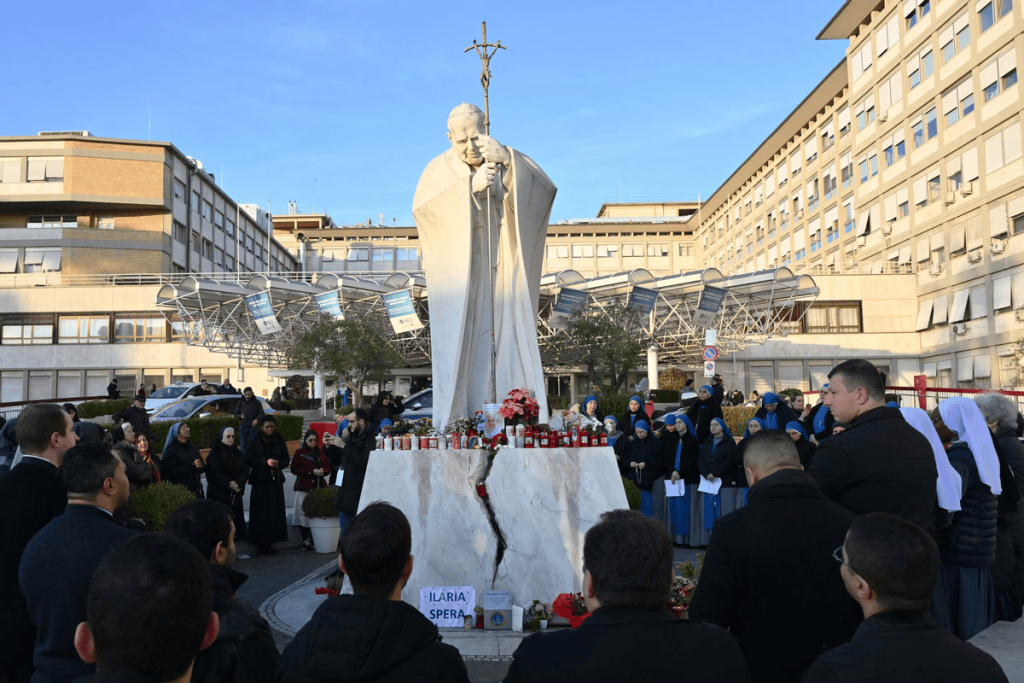 People pray at the statue of John Paul II outside the Gemelli hospital where Pope Francis is hospitalized in Rome, on Feb. 22, 2025. (Image Credit: Alberto Pizzoli / AFP)