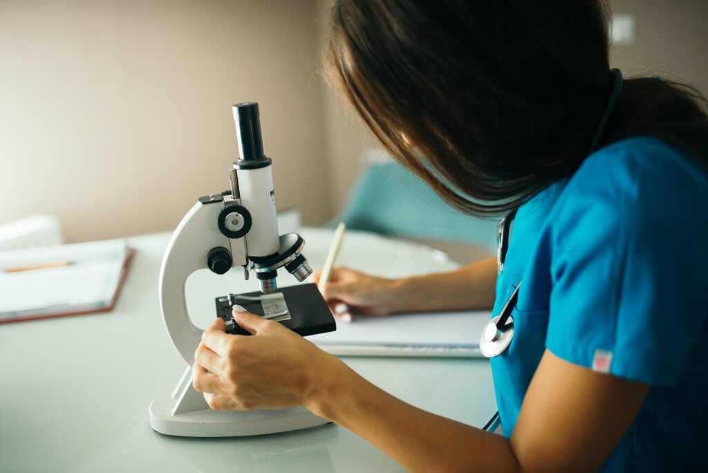 Close up of a nurse using a microscope and writing down notes