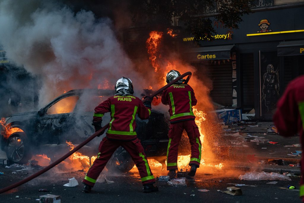 Paris riots, 17 October 2026   Firefighters extinguishing a burning car   JJxFile