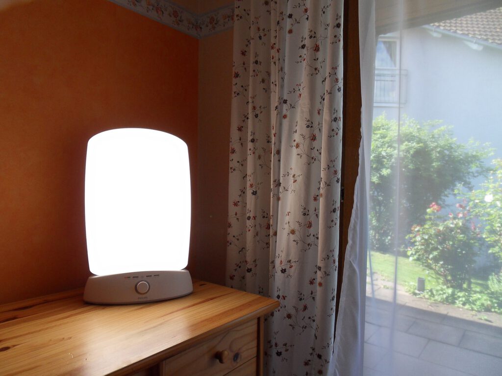 A modern SAD lamp emitting bright light on a desk next to a window
