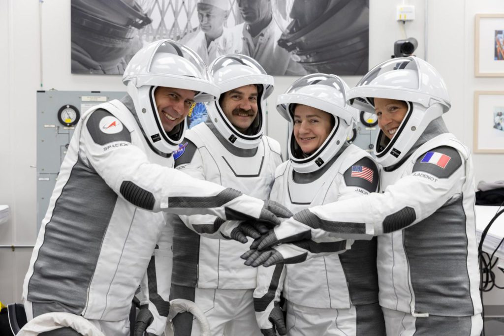 NASA’s SpaceX Crew-12 astronauts stand side by side in their spacesuits with face shields raised. They extend their arms forward, stacking their hands together in a team huddle while smiling. Pictured at the Neil A. Armstrong Operations and Checkout Building at Kennedy Space Center ahead of their Feb. 13, 2026 launch to the International Space Station, from left to right: Roscosmos cosmonaut Andrey Fedyaev, NASA astronauts Jack Hathaway and Jessica Meir, and ESA astronaut Sophie Adenot.