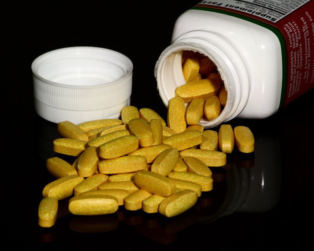 A glass of water and a bottle of vitamin supplements next to a toilet bowl showing neon yellow urine