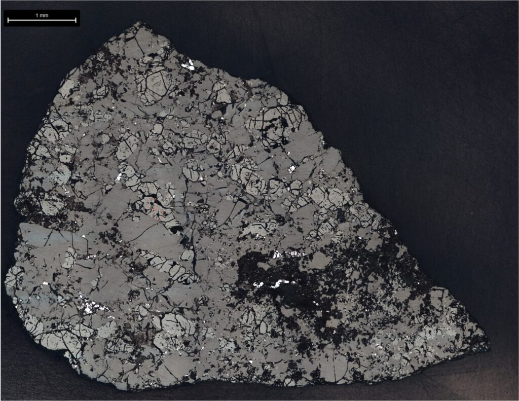A microscopic cross-section of a rock specimen set against a black background, displaying a heavily fractured, mosaic-like mineral texture in shades of gray and black with a 1-millimeter scale bar in the top-left corner.