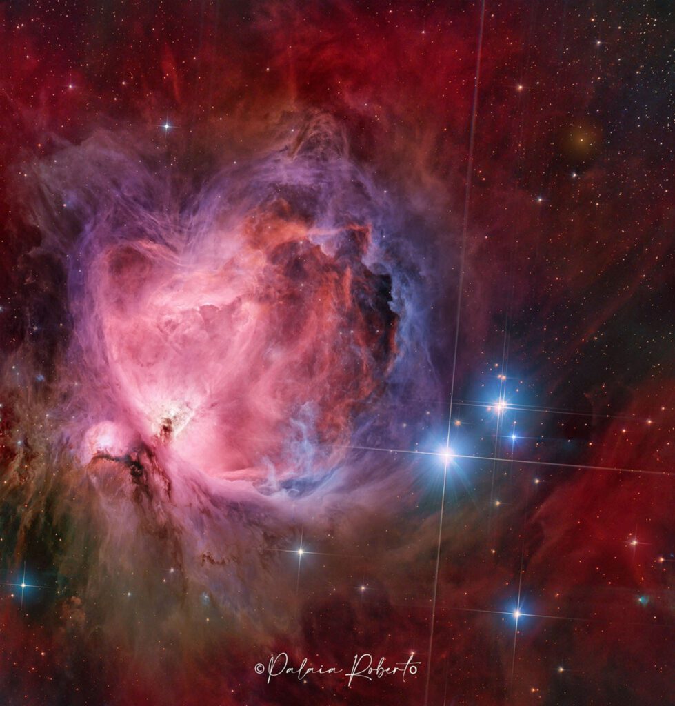 Orion Nebula M42 Featured as Star-Birth Region 1 A starfield features a large and colorful nebula in its center, filled with dark dust and glowing gas in red and blue.