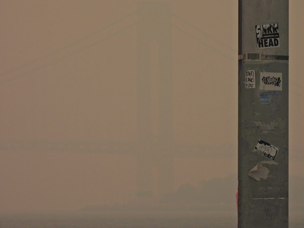 The Verrazano Narrows bridge barely visible through heavy wildfire smoke juxtaposed by a nearby pole