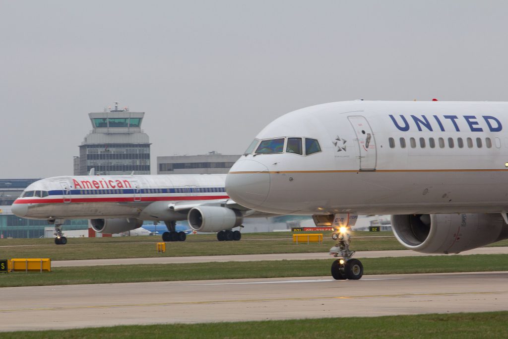 Passengers waiting at a busy transatlantic airport terminal with flight information displays