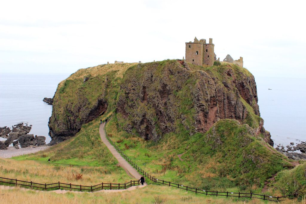 Ruined stone arches of an ancient castle on a cliff edge overlooking the sea at dusk