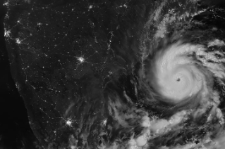 A nighttime satellite image shows Arnab's circular structure with bright white clouds as the storm approaches India's east coast. City lights are visible on darkened land surfaces on the left side of the image.